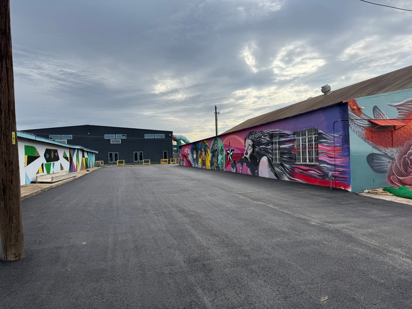 Fresh commercial asphalt paving between mural-covered buildings